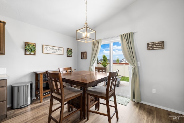 dining space with baseboards, a notable chandelier, light wood-style flooring, and lofted ceiling