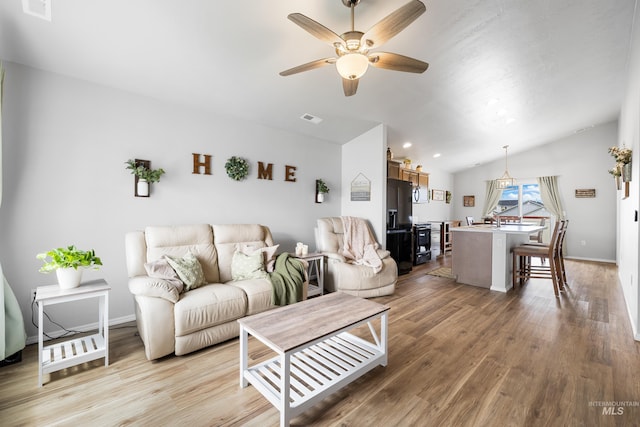 living room with a ceiling fan, vaulted ceiling, light wood-style flooring, and visible vents