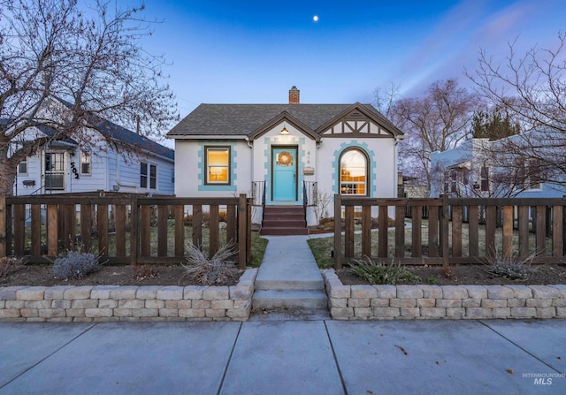 view of front of property with a fenced front yard, stucco siding, a chimney, and a shingled roof