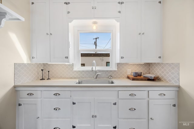 kitchen featuring tasteful backsplash, white cabinetry, light countertops, and a sink