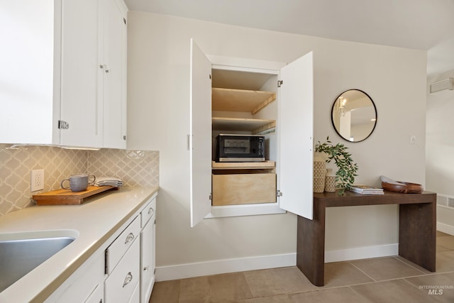 kitchen with tasteful backsplash, white cabinets, light countertops, light tile patterned floors, and baseboards