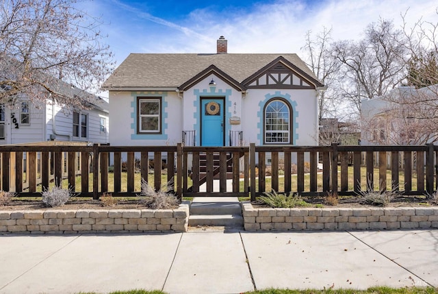 view of front facade featuring a chimney, stucco siding, a shingled roof, and a fenced front yard