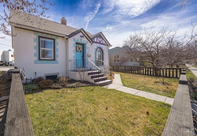 view of front of house featuring stucco siding, fence, a front yard, a shingled roof, and a chimney