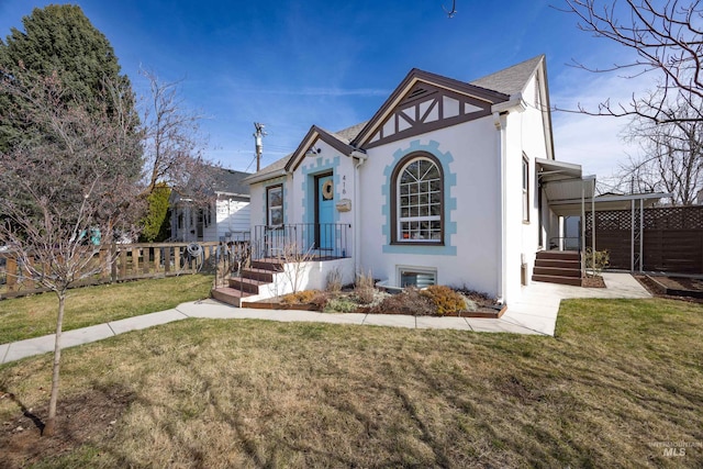 tudor home featuring a front lawn, fence, and stucco siding