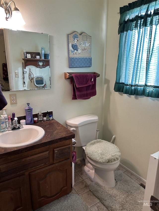 half bath with vanity, toilet, baseboards, and tile patterned flooring