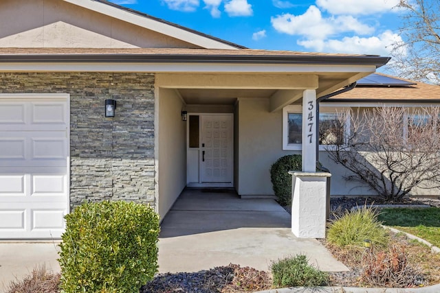 entrance to property with an attached garage, stone siding, roof mounted solar panels, and stucco siding