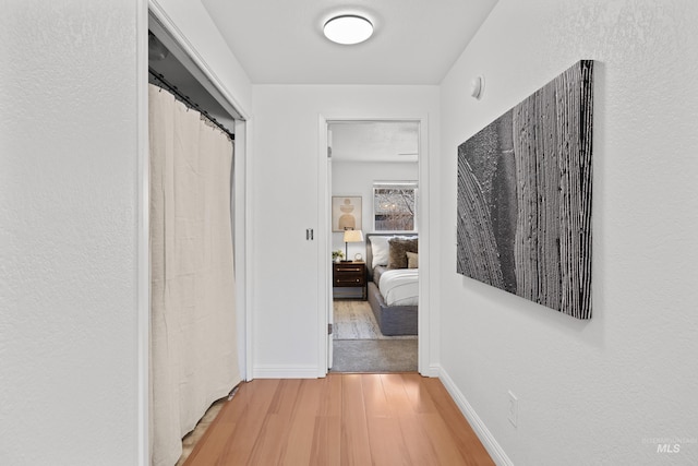 corridor featuring light wood-style flooring and baseboards