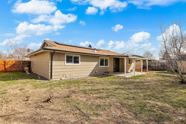 rear view of property featuring solar panels, a patio area, a lawn, and a fenced backyard