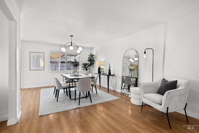 dining area with baseboards, a notable chandelier, a textured ceiling, and light wood-style floors