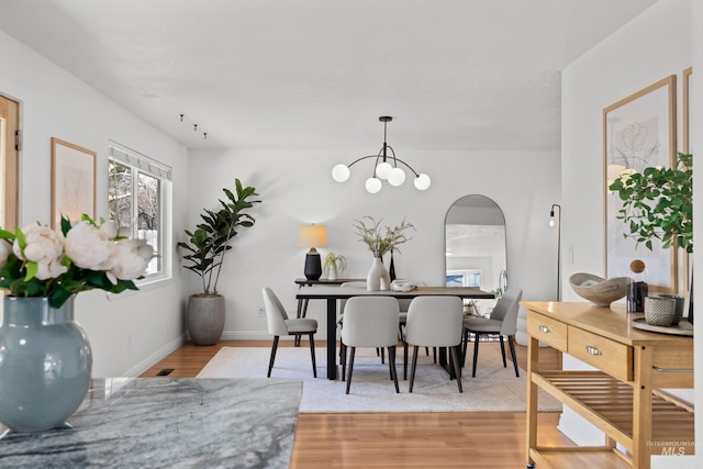 dining area featuring light wood finished floors, a chandelier, arched walkways, and baseboards