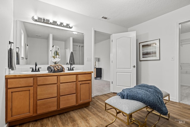bathroom with a textured ceiling, visible vents, wood finished floors, a sink, and double vanity