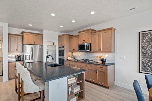 kitchen with a center island with sink, backsplash, light hardwood / wood-style flooring, stainless steel appliances, and sink