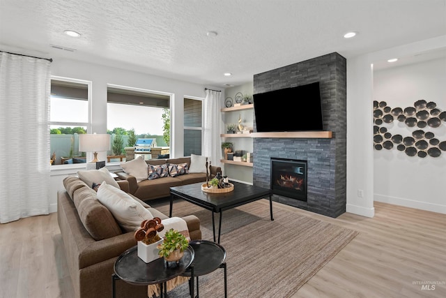 living room with light hardwood / wood-style flooring, a stone fireplace, and a textured ceiling