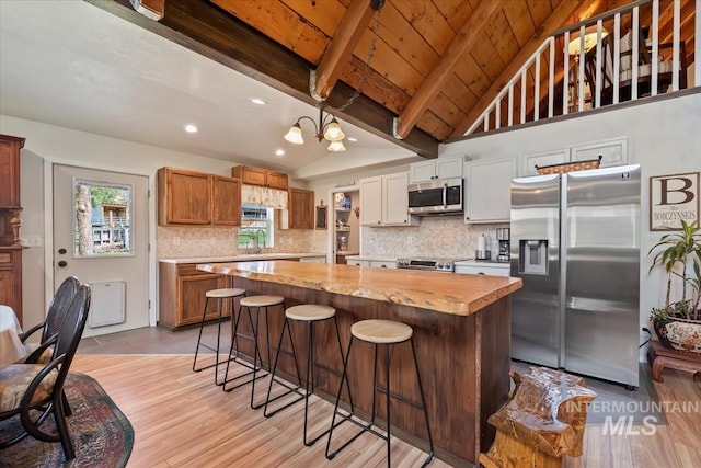 kitchen with a kitchen island, appliances with stainless steel finishes, vaulted ceiling with beams, and light wood-style floors