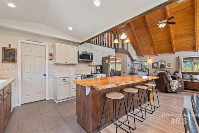 kitchen with vaulted ceiling, stainless steel appliances, white cabinetry, and open floor plan