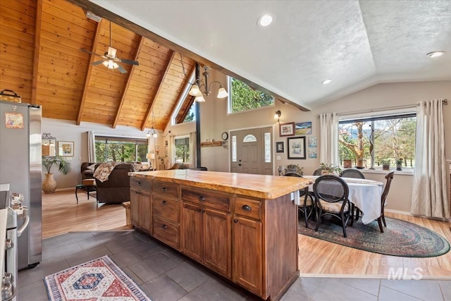 kitchen with brown cabinetry, freestanding refrigerator, open floor plan, vaulted ceiling with beams, and dark tile patterned flooring