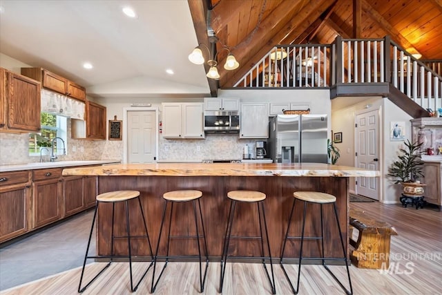 kitchen with a kitchen island, backsplash, appliances with stainless steel finishes, vaulted ceiling, and a sink