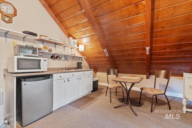 kitchen with fridge, light colored carpet, wooden ceiling, vaulted ceiling with beams, and white microwave