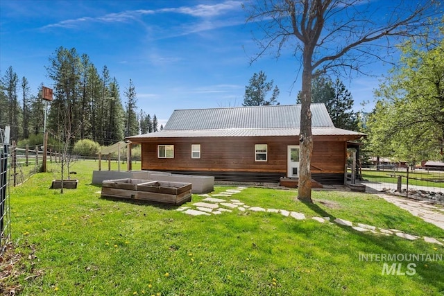 rear view of property with a lawn, fence, metal roof, and a vegetable garden