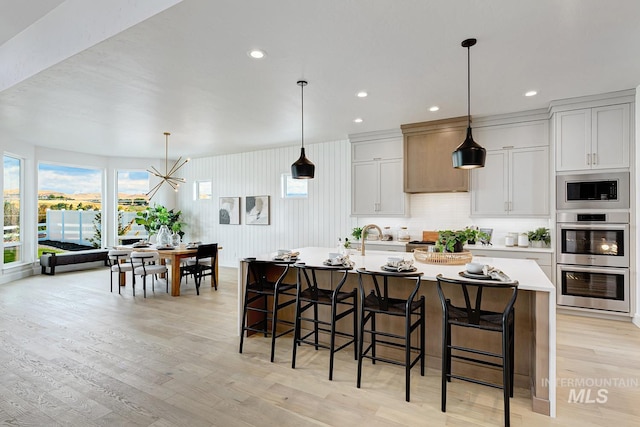 kitchen featuring a kitchen breakfast bar, light wood-type flooring, a center island with sink, light countertops, and appliances with stainless steel finishes