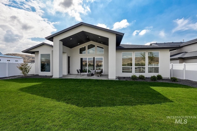 back of house with fence, stucco siding, a yard, and a patio area