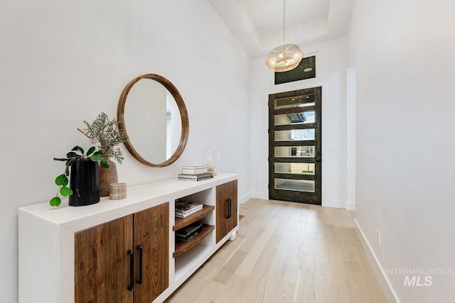 interior space with a tray ceiling, a notable chandelier, baseboards, and light wood-type flooring