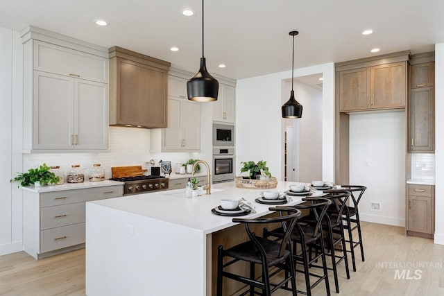 kitchen featuring light wood-style flooring, a sink, appliances with stainless steel finishes, light countertops, and backsplash