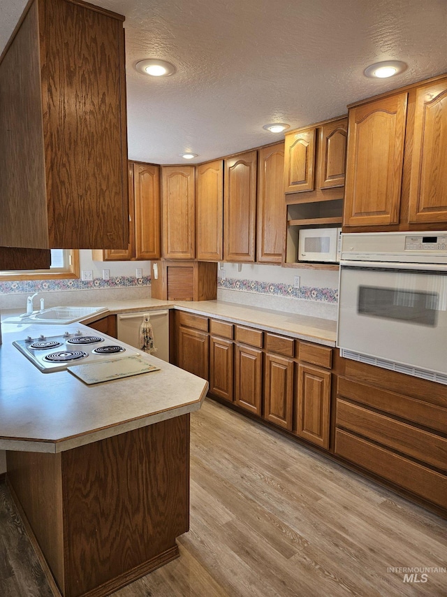 kitchen with white appliances, light wood-type flooring, a textured ceiling, sink, and kitchen peninsula