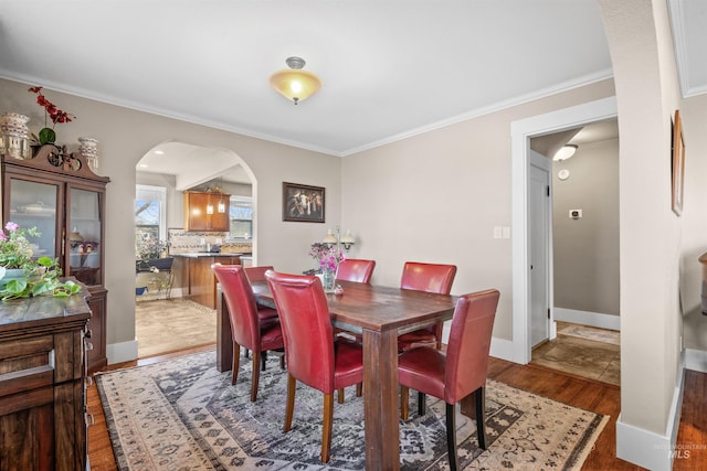 dining space featuring arched walkways, crown molding, and light wood finished floors