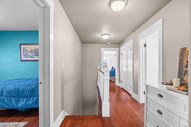 hallway with wood finished floors, an upstairs landing, and baseboards