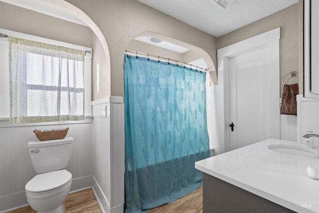 bathroom featuring a wainscoted wall, a shower with shower curtain, wood finished floors, and toilet