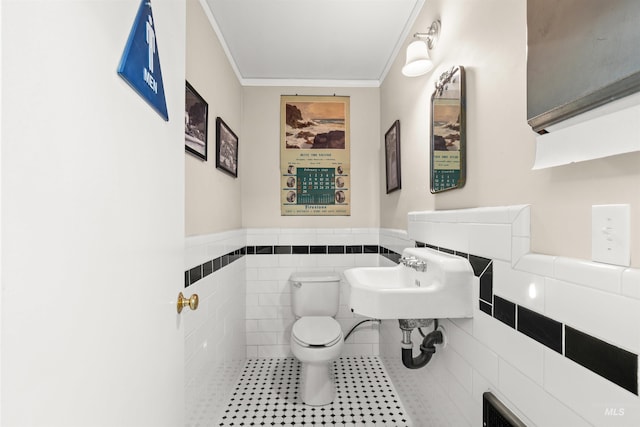 half bathroom featuring tile walls, toilet, ornamental molding, wainscoting, and tile patterned flooring