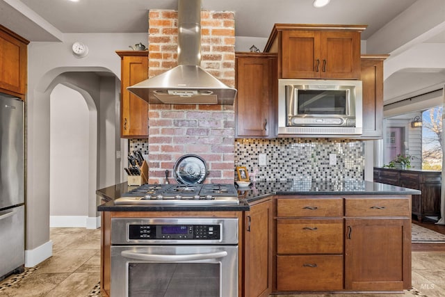 kitchen with stainless steel appliances, wall chimney range hood, dark countertops, and decorative backsplash