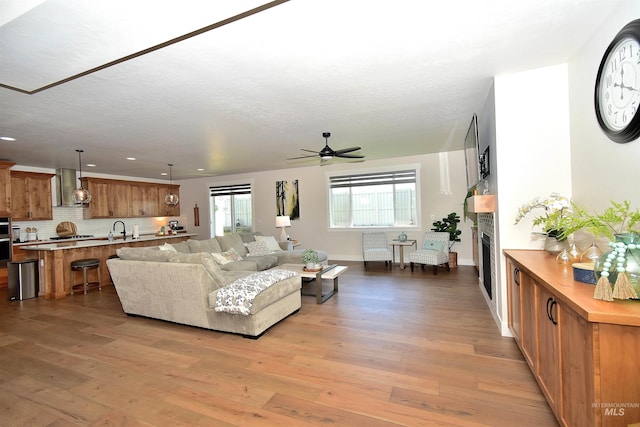 living room with light wood-type flooring, ceiling fan, and sink