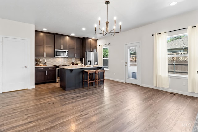 kitchen with appliances with stainless steel finishes, wood finished floors, dark brown cabinetry, a breakfast bar, and a chandelier