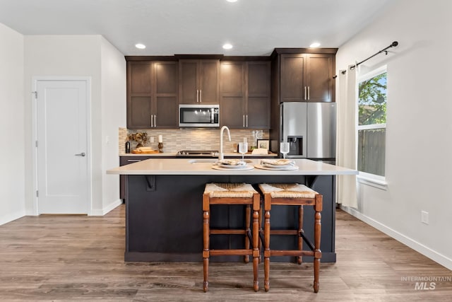 kitchen featuring stainless steel appliances, dark brown cabinetry, a breakfast bar area, wood finished floors, and recessed lighting
