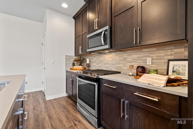 kitchen featuring appliances with stainless steel finishes, dark brown cabinetry, light countertops, dark wood-style floors, and tasteful backsplash