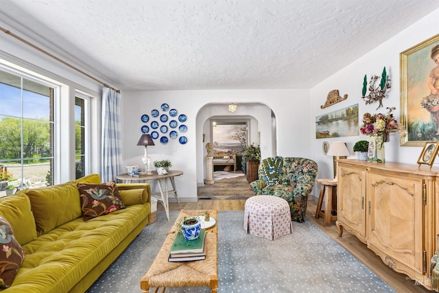 living room featuring arched walkways, a textured ceiling, and wood finished floors