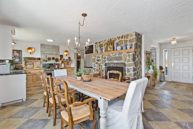 dining area with a textured ceiling, an inviting chandelier, and a stone fireplace