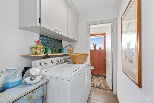clothes washing area with separate washer and dryer, light wood-type flooring, and cabinet space