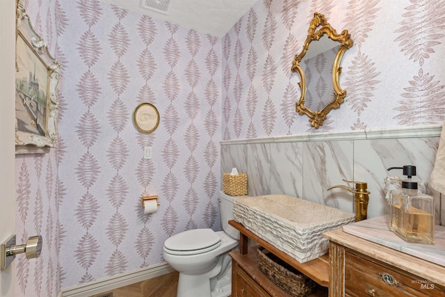 half bathroom with toilet, wallpapered walls, and visible vents