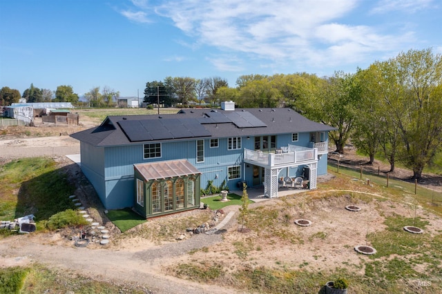 back of property featuring a wooden deck, roof mounted solar panels, a patio area, an outdoor fire pit, and an outbuilding