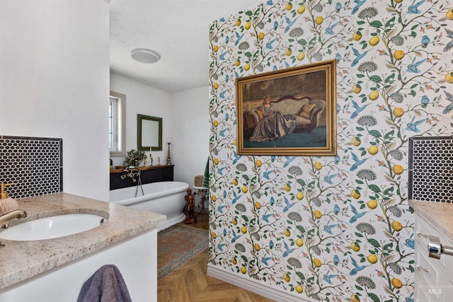 bathroom with a sink, a freestanding bath, wallpapered walls, and two vanities