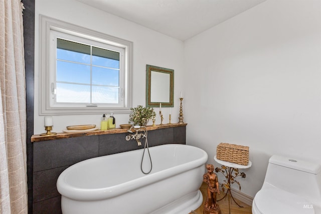 full bathroom featuring baseboards, a freestanding bath, and toilet