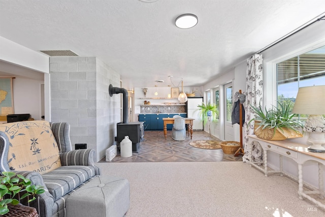 living room with visible vents, a wood stove, a textured ceiling, and light carpet