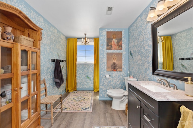 bathroom featuring visible vents, vanity, wood finished floors, toilet, and wallpapered walls