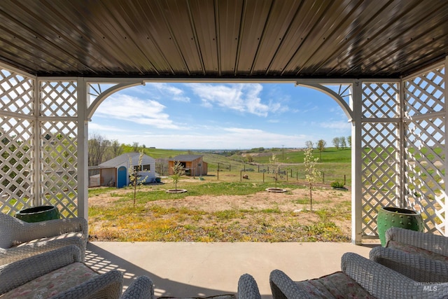 view of patio / terrace with an outdoor fire pit, fence, an outdoor structure, a storage unit, and a rural view