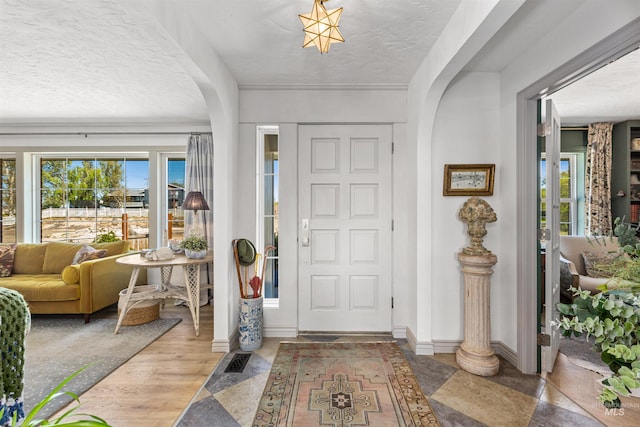 foyer featuring arched walkways, baseboards, plenty of natural light, and a textured ceiling