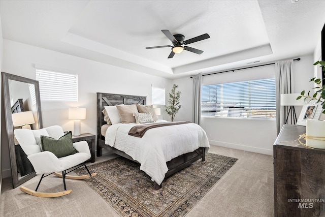 bedroom featuring baseboards, a raised ceiling, light colored carpet, and ceiling fan