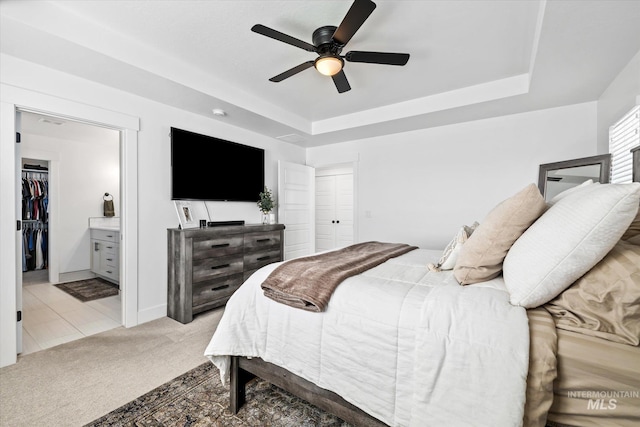 carpeted bedroom featuring a closet, a raised ceiling, connected bathroom, and a ceiling fan